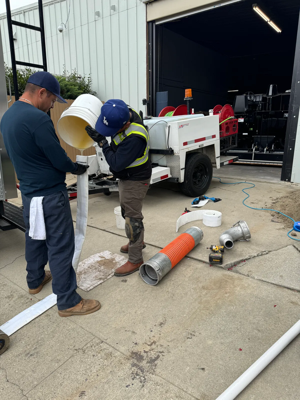 Two Trifecta technicians saturating a CIPP pipe liner with resin beside a trailer-mounted hydro jetter