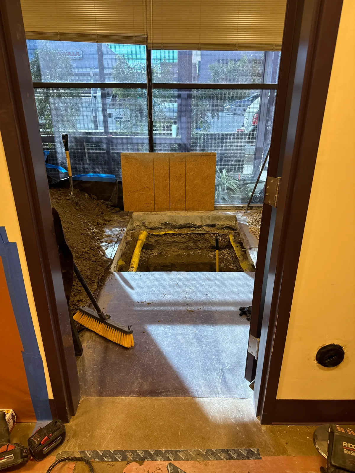 Interior under-slab excavation exposing new sewer piping just inside a commercial tenant entrance